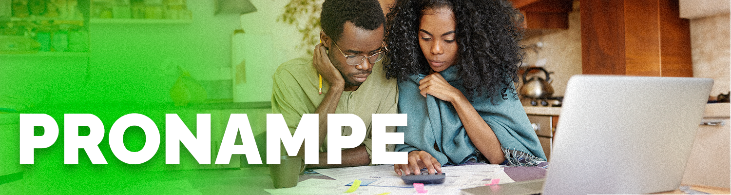 Um homem e uma mulher negros olhando para um papel e estão em frente ao um notebook e escrito em cima pronampe