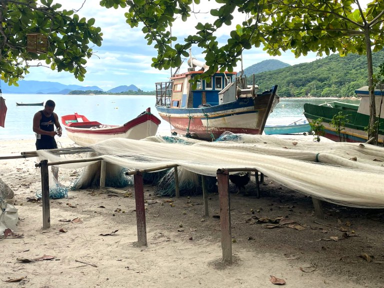 Imagem de pescador consertando sua rede em frente à praia