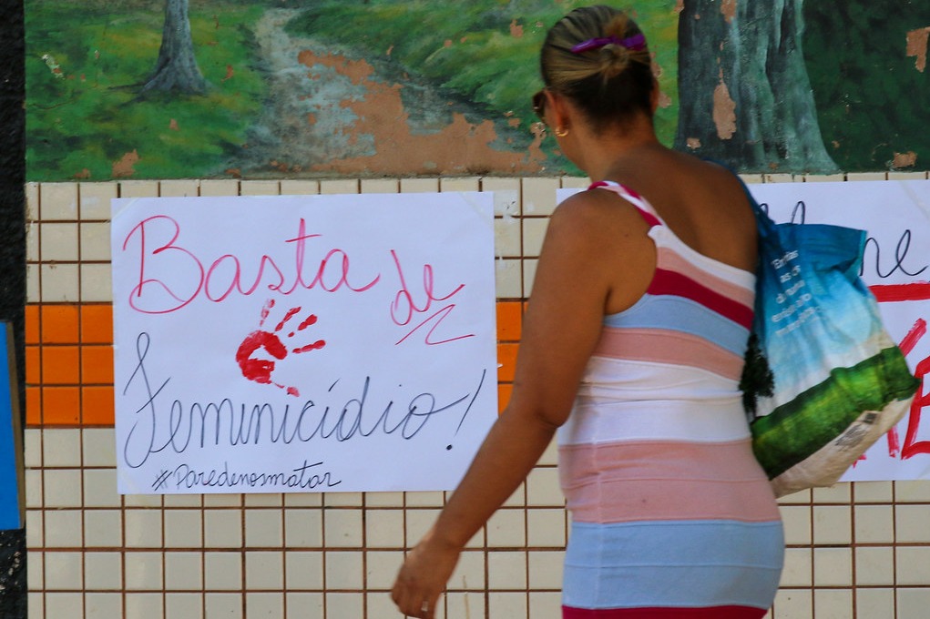 Mulher olha cartaz em um mural nba rua com a manifestção: Basa de feminicídio.. Pare de nos matar e símbolo de basta com pintura d Hastag parede nosmata