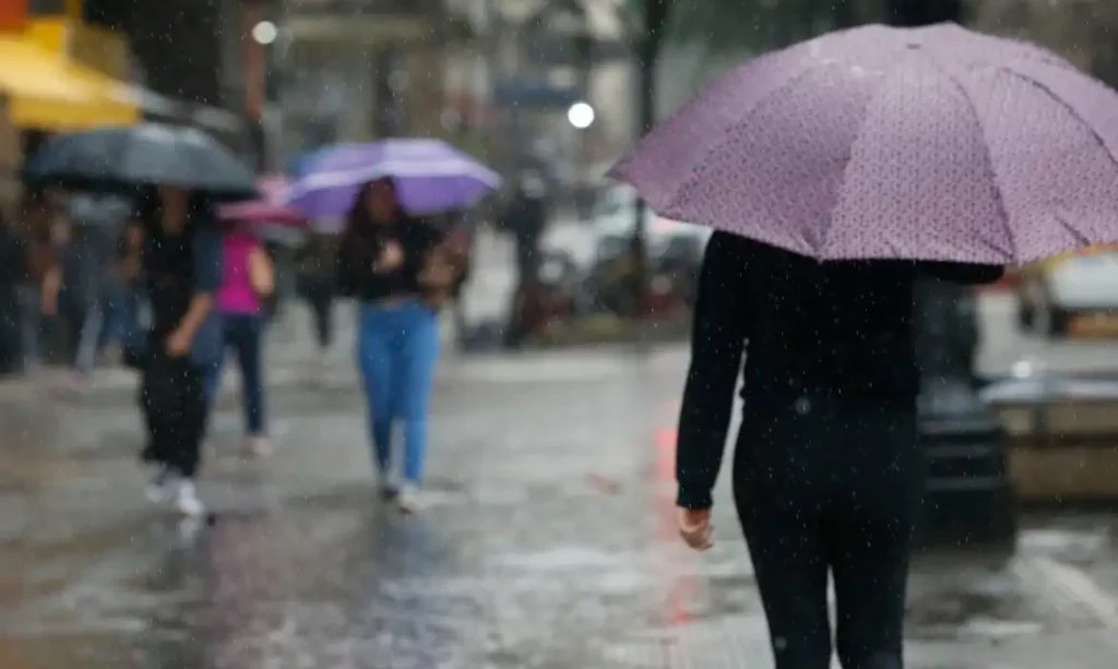 Mulher caminha na chuva com sombrinha