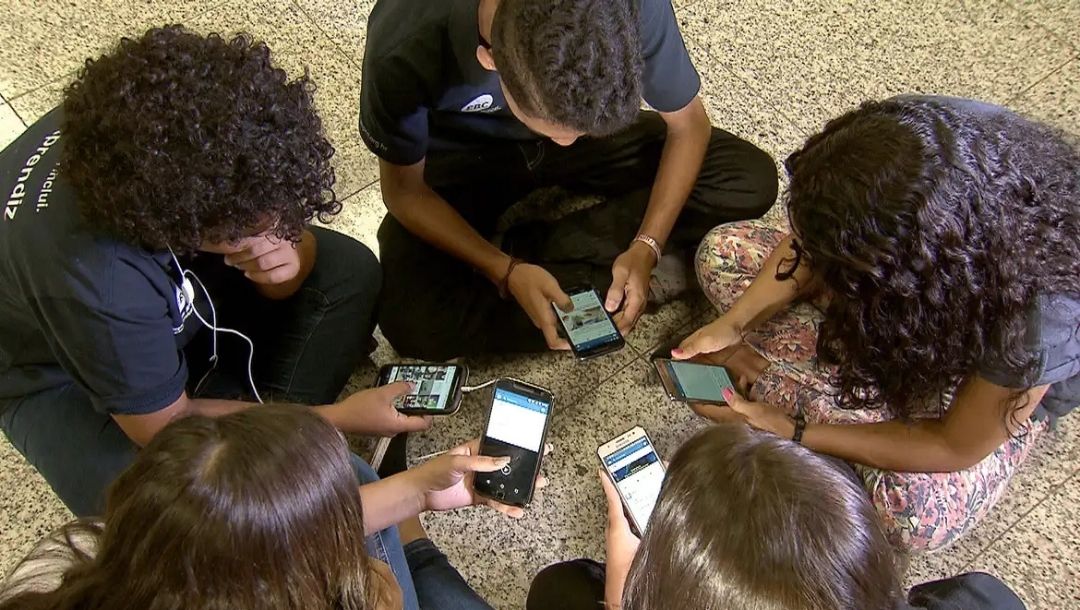 Roda de meninas e meninos usando celular