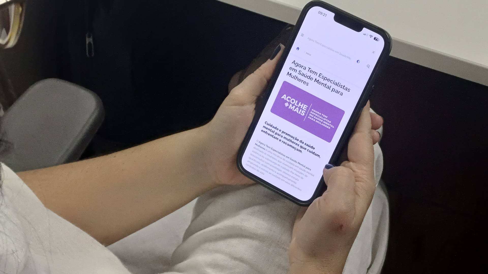 Foto de um mulher segurando um celular com o Programa AcolheMais, do SUS, aparecendo na tela.