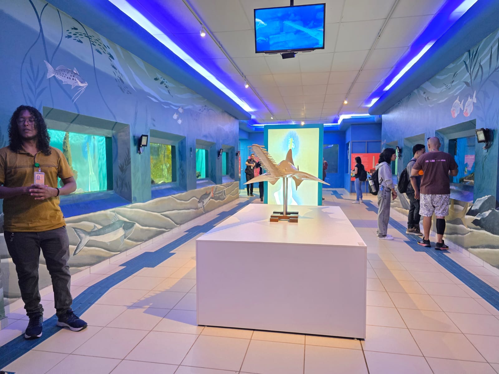Parte interna de prédio do aquário com exposições e pessoas