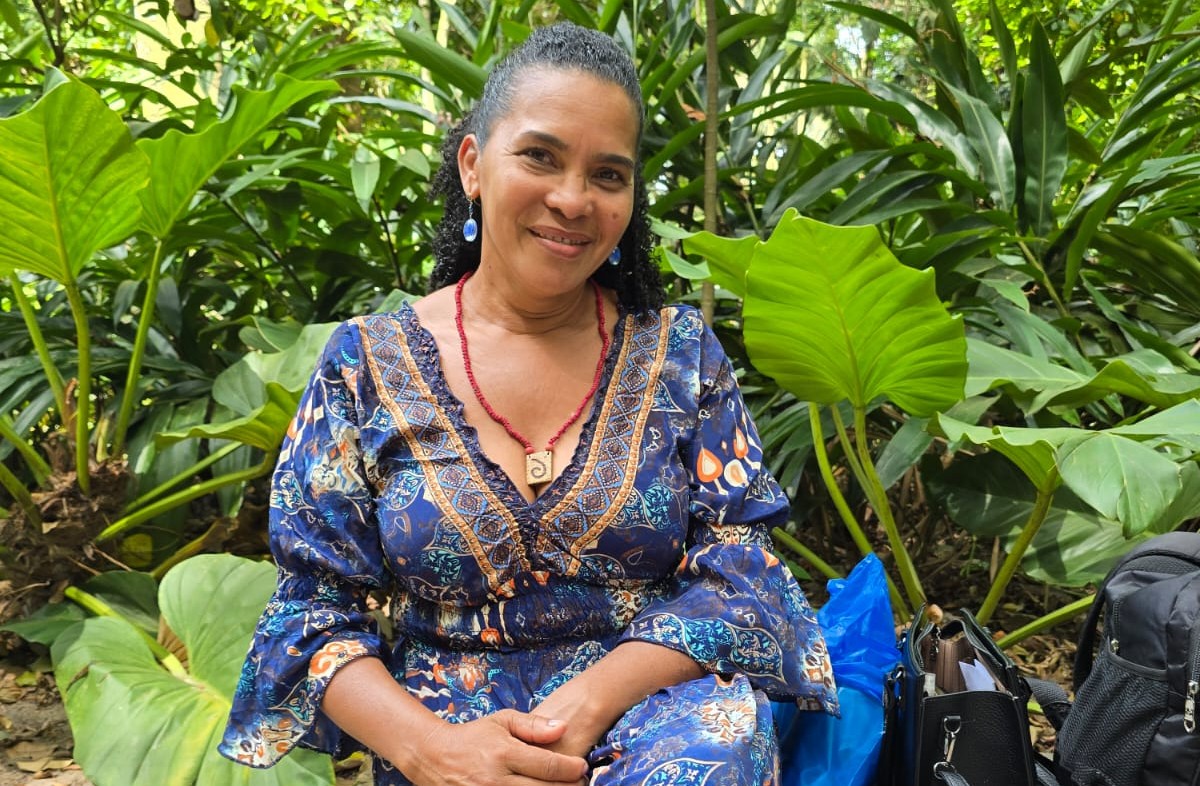 Mulher negra sentada em um banco de um parque com vegetação verde e vibrante