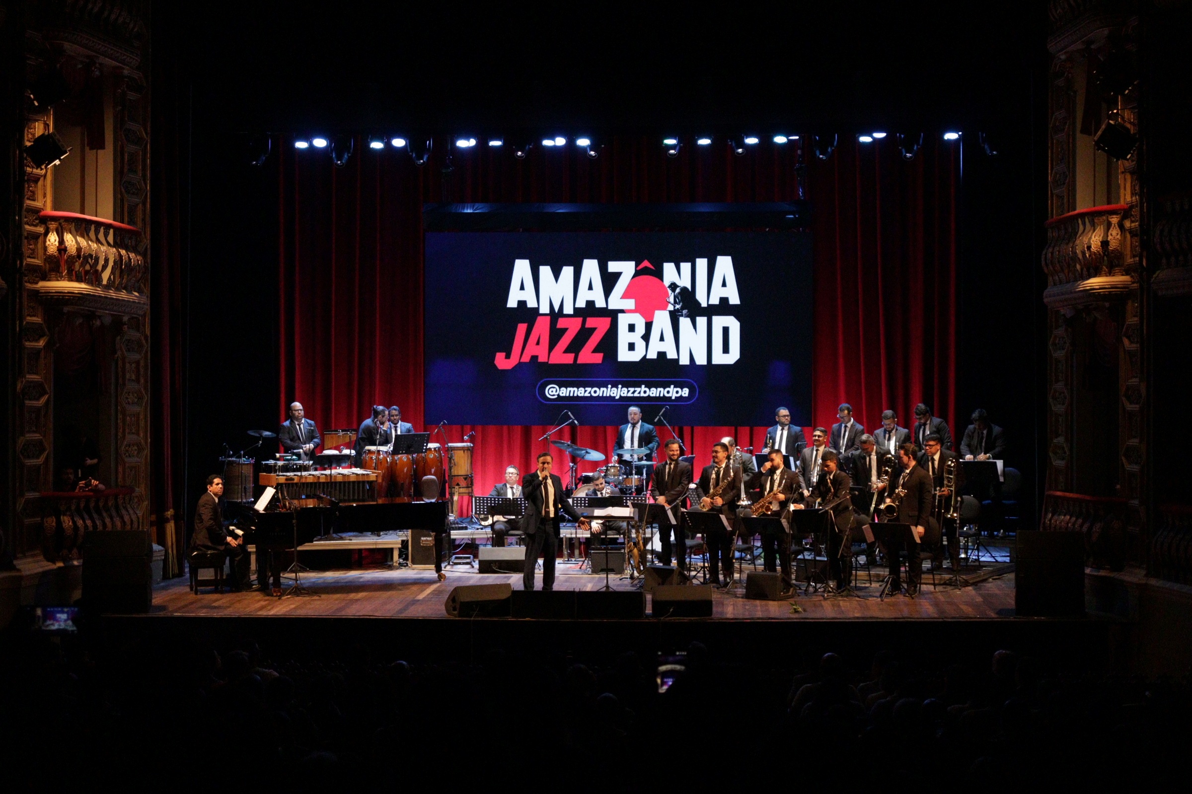 homem de terno à frente de orquestra em teatro