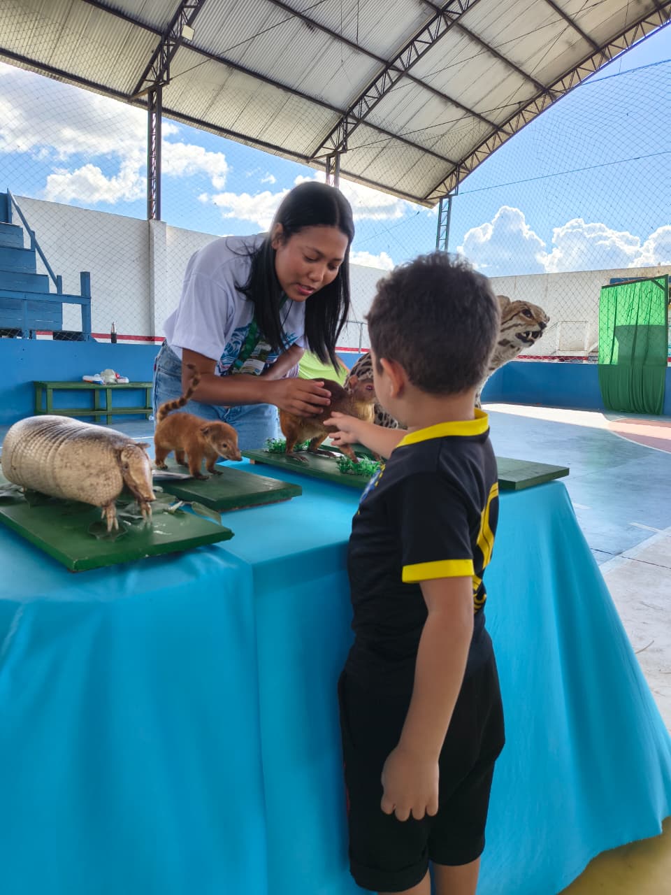 Uma pesquisadora apresenta mamíferos a uma criança, que toca e interage com a apresentação