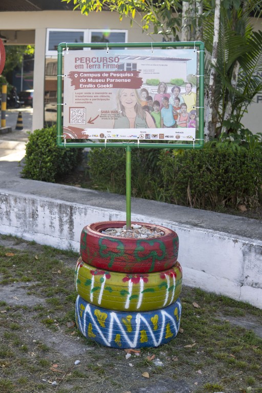 Um totem feito com canos e pneus traz a imagem de uma mulher loira sorridente em frente ao Campus