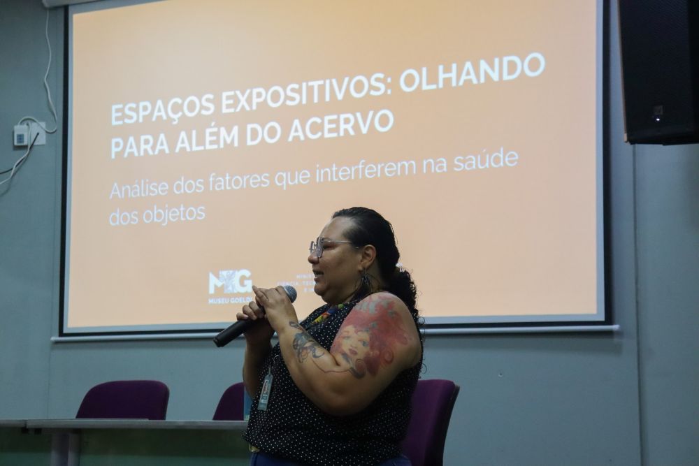 Mulher segurando microfone apresenta slides projetados em telão