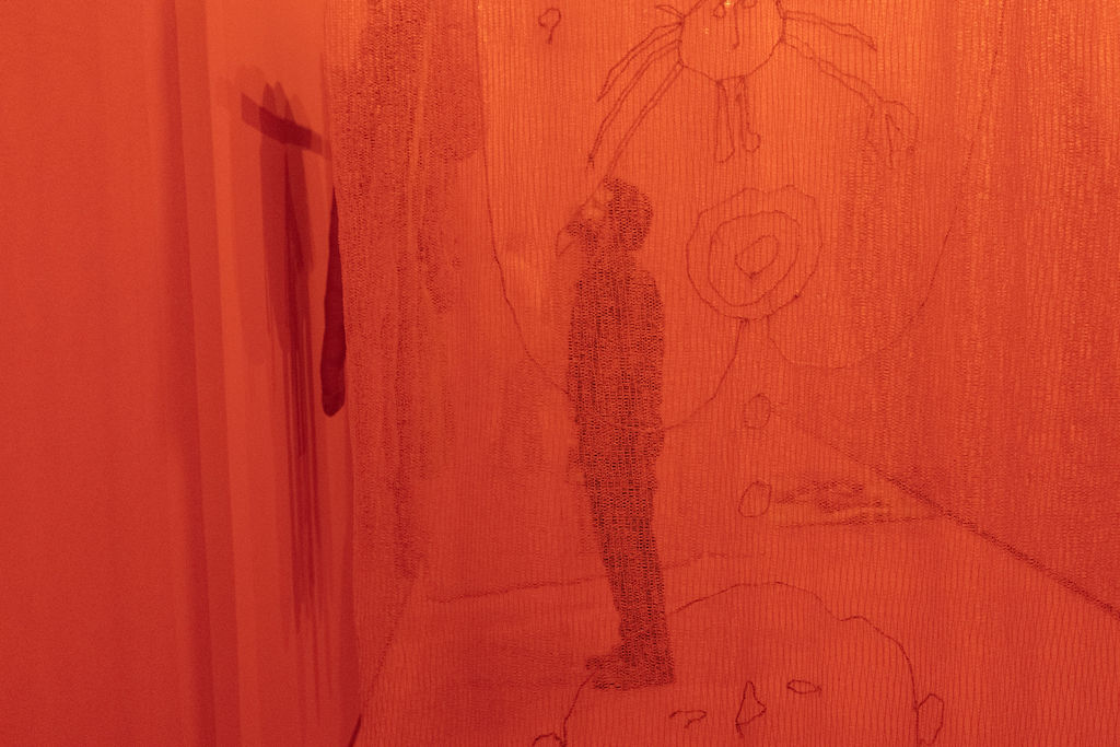 silhueta de homem em pé é vista através de cortina vermelha de instalação artística