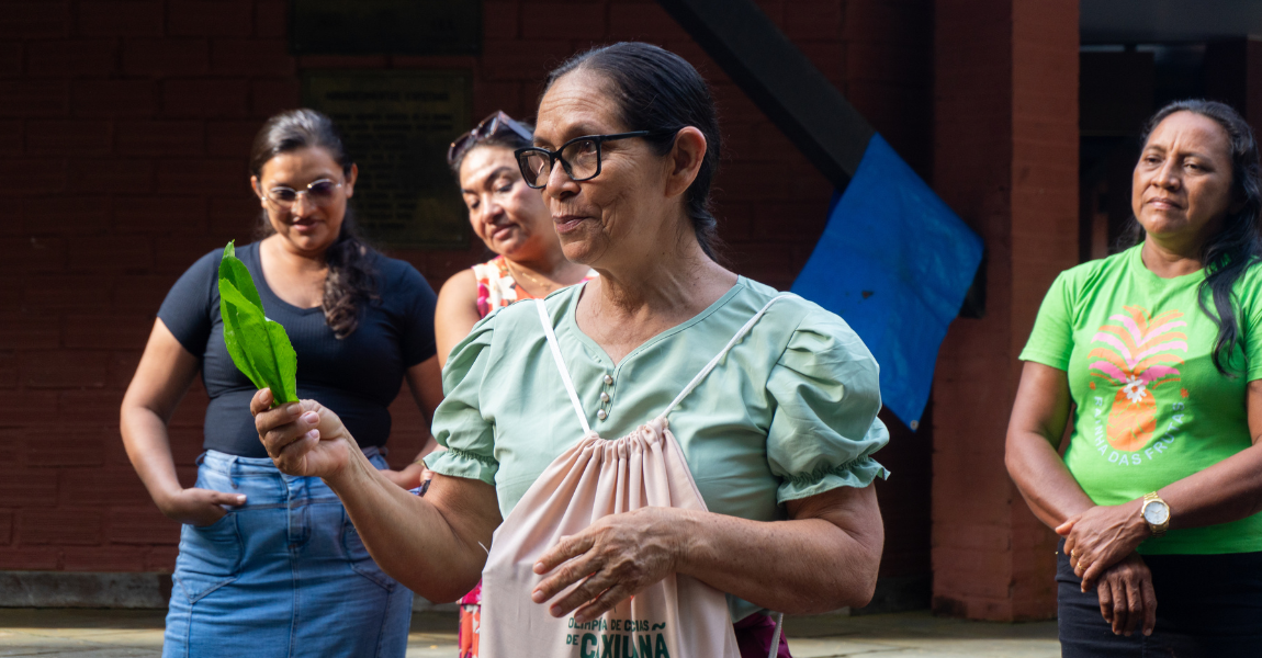Uma senhora segura uma folha em um ambiente ao ar livre durante aula sobre restauração biocultural