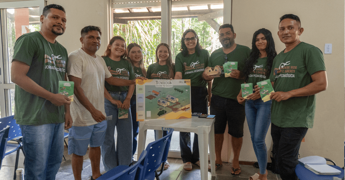 Professores ao redor de uma mesa seguram um cartaz com a frase "tecnologias sociais na escola"