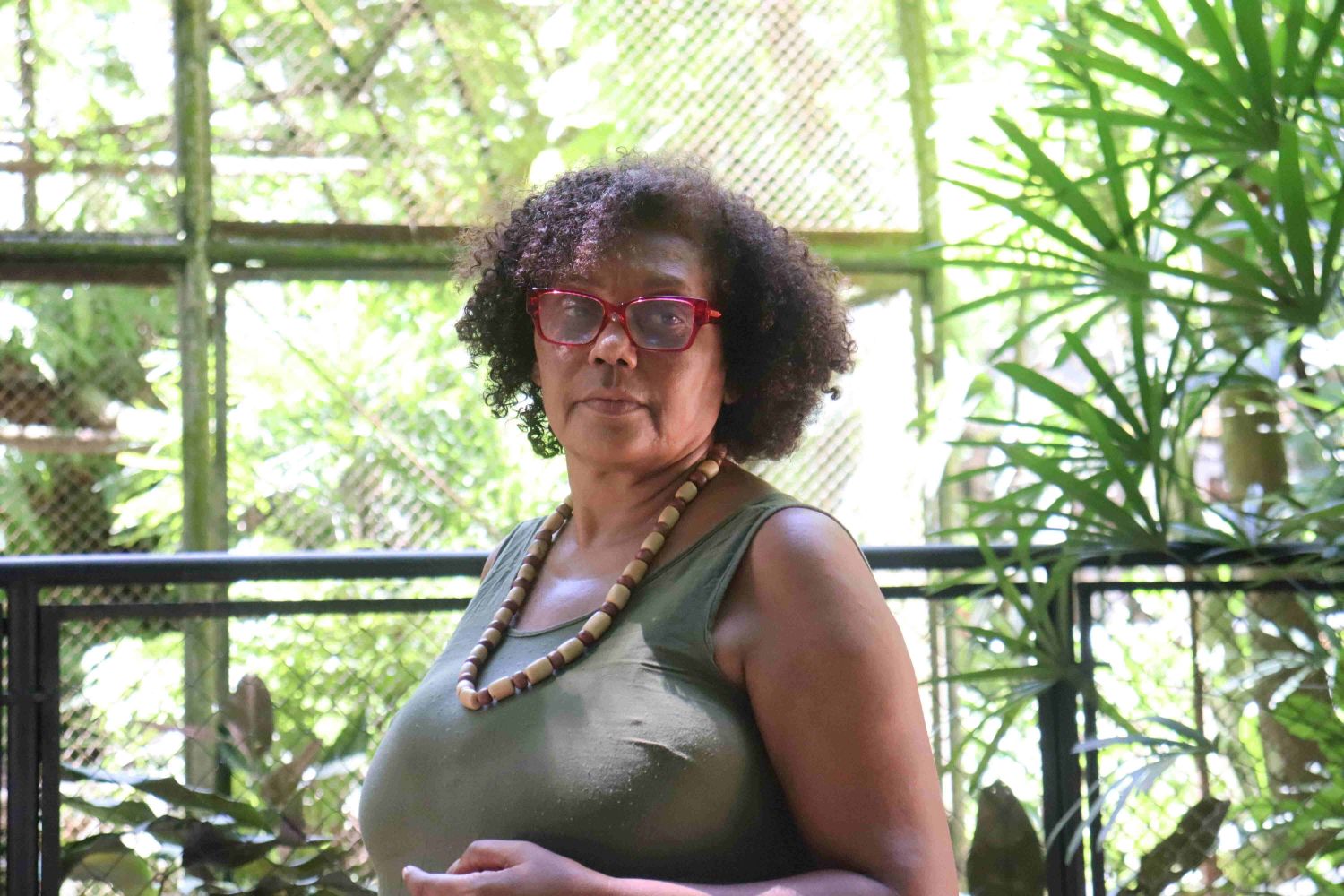 Uma pesquisadora negra posa para foto usando óculos vermelho, colar de miçanga e camiseta verde