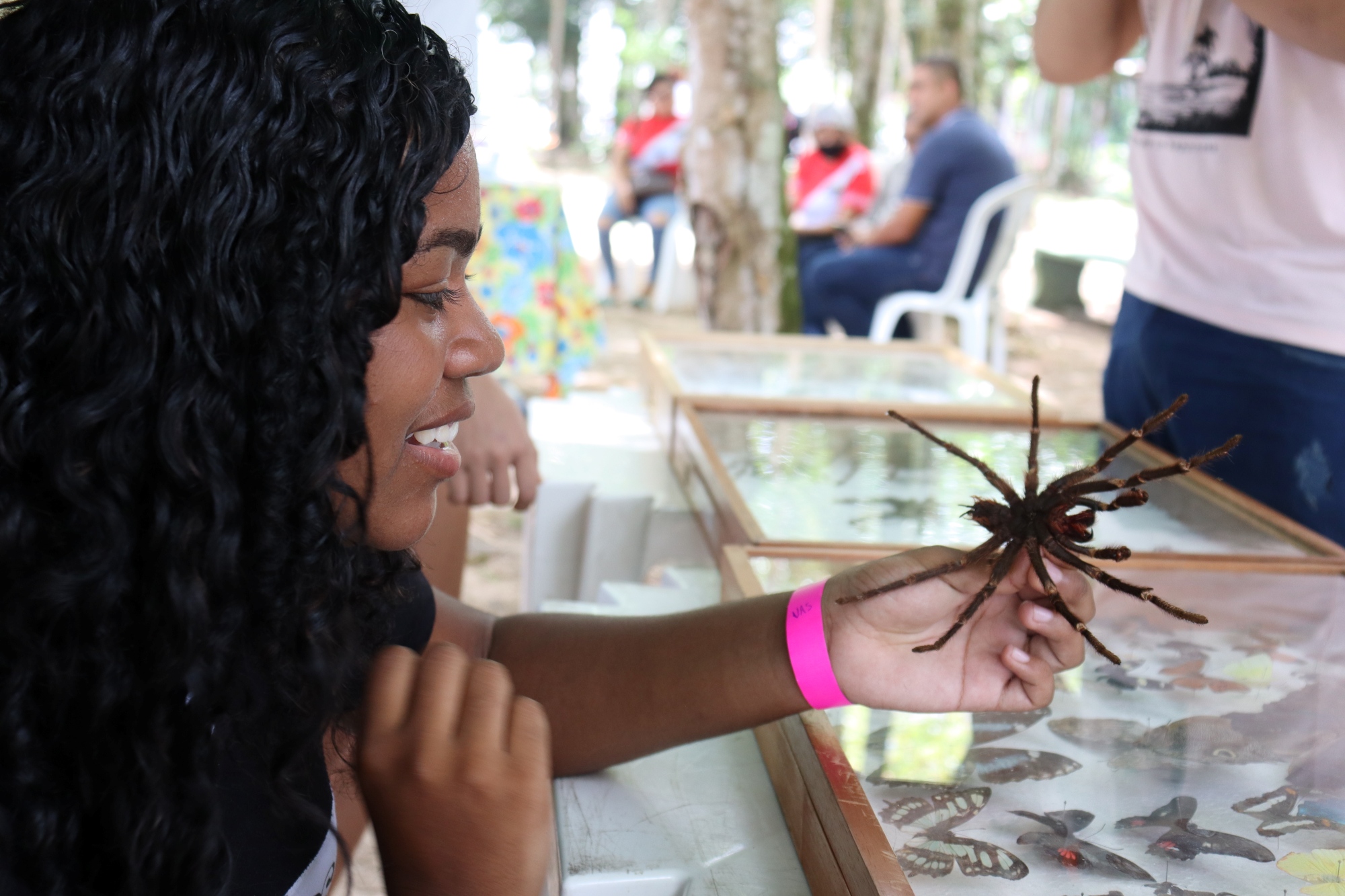 Menina de cabelos cacheados sorri enquanto segura uma grande aranha pelas patas