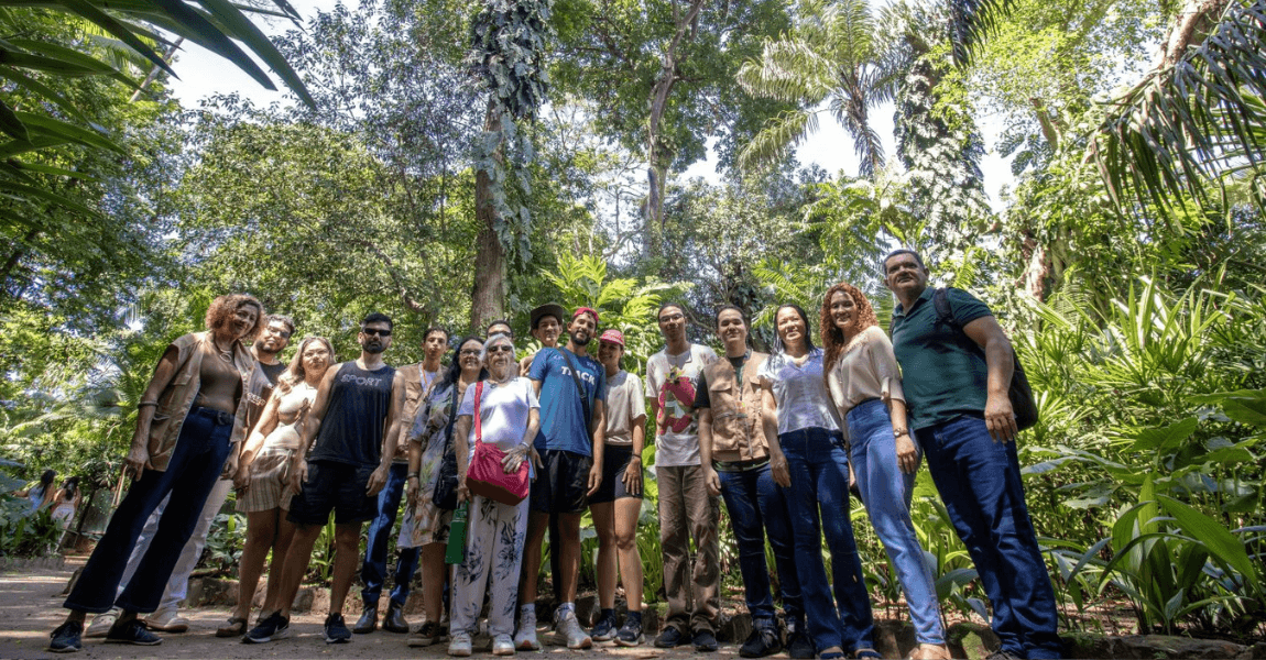 Grupo de pessoas posam para foto diante de uma árvore de grande porte num parque zoobotânico