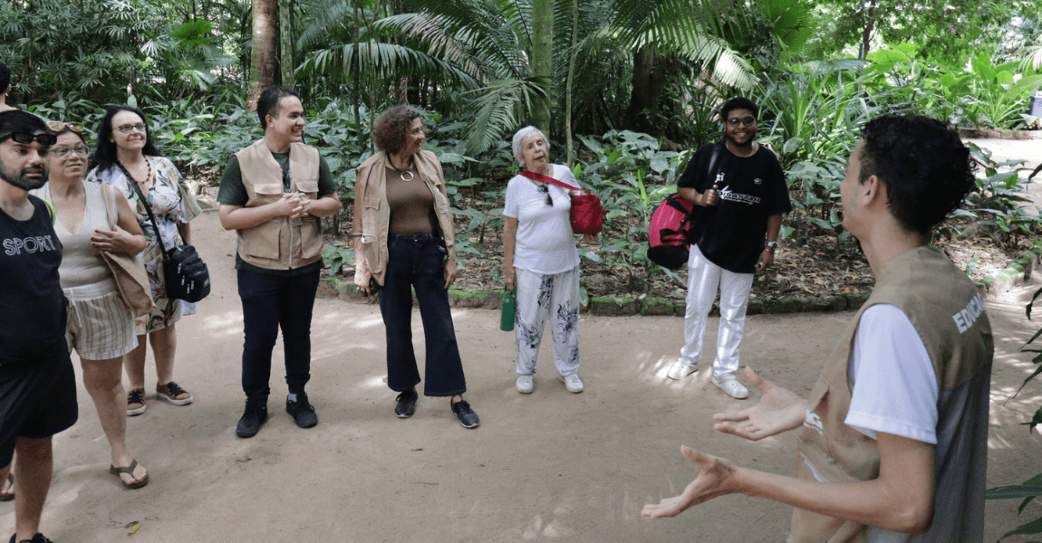 Um guia turístico usando colete fala para um grupo numa área verde
