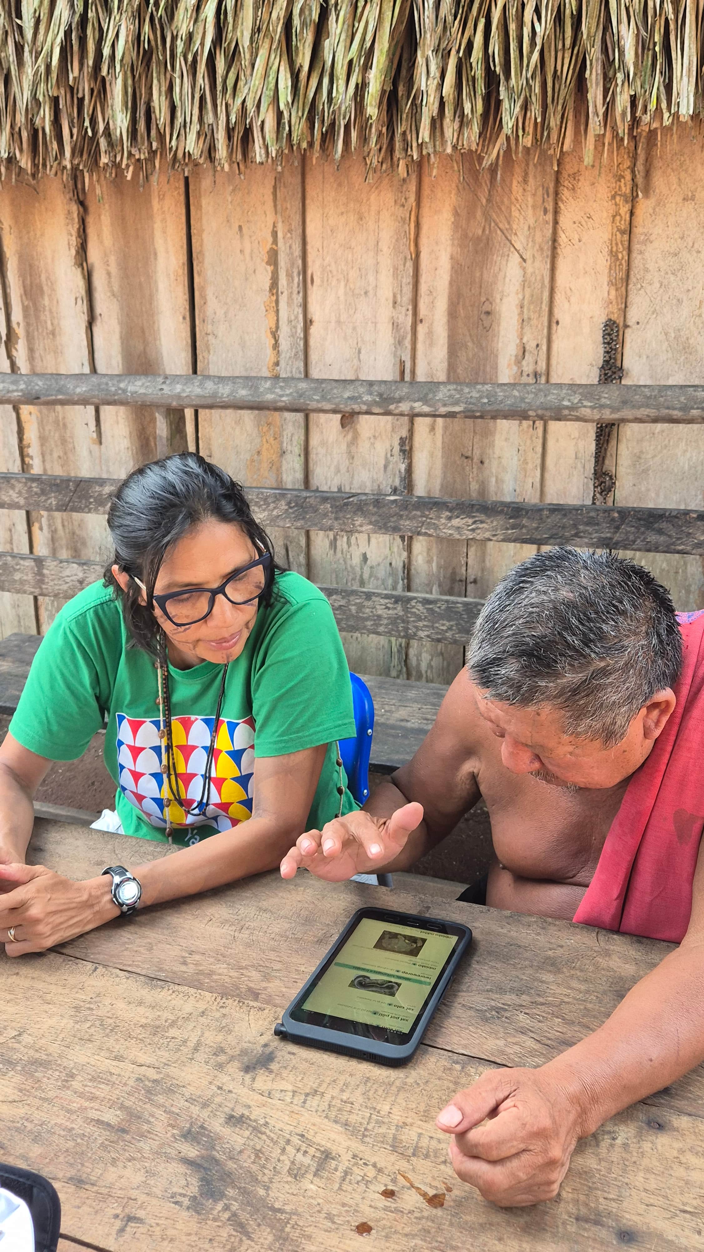 Mulher sentada ao lado de homem de cabelos brancos, que está de cabeça baixa usando tablet