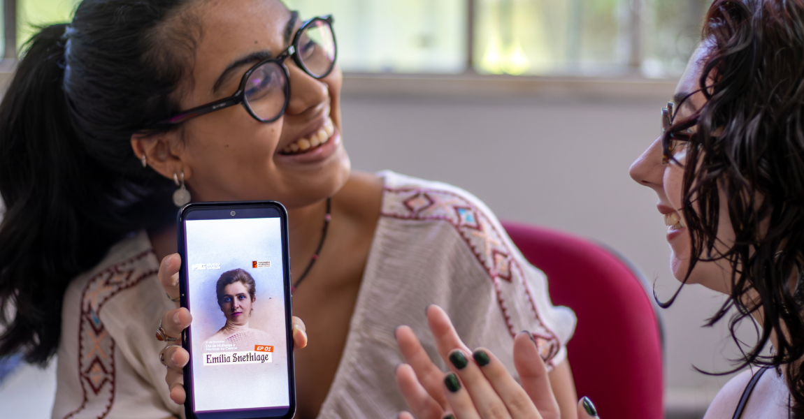 Uma jovem mostra tela de celular com imagem de pesquisadora à colega