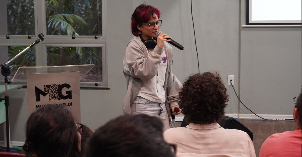 Uma jovem de cabelos vermelhos fala ao microfone em auditório