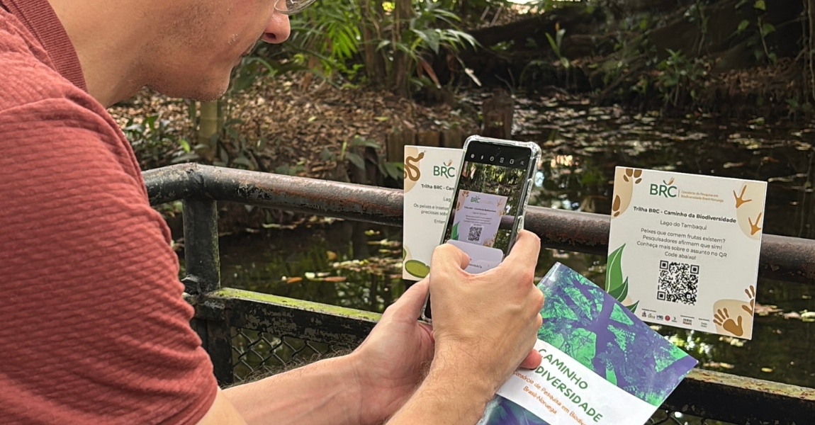 homem aponta celular para placa que contém QR code afixada no mural de um lago
