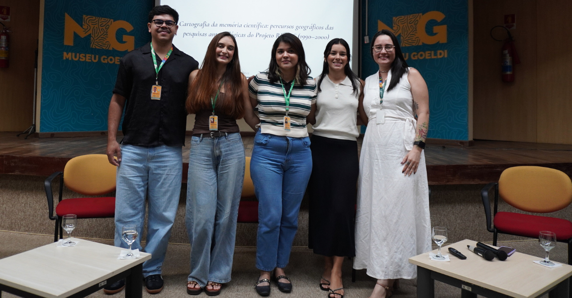 Um homem e quatro mulheres com crachas num auditório posam para foto