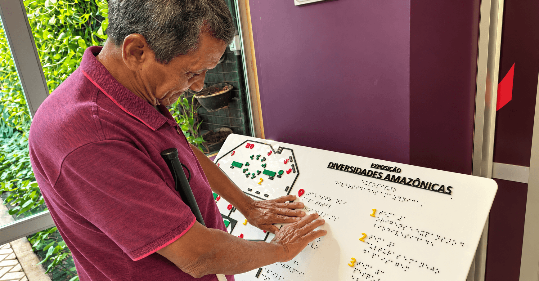 Um homem com deficiência visual toca um mapa tátil em frente a uma exposição