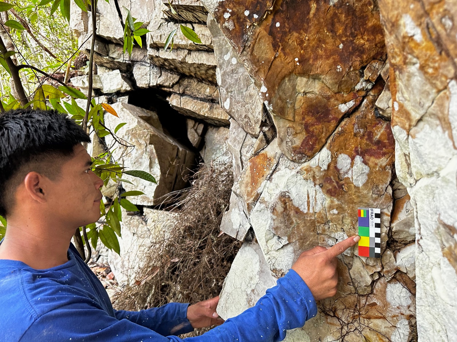 Homem indígena jovem coloca escala de cores perto de pinturas em rocha