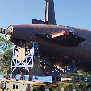 Imagem da galeria de imagem da página de Defesa. A imagem mostra a rabeta de um submarino em construção na parte externa de uma fábrica.