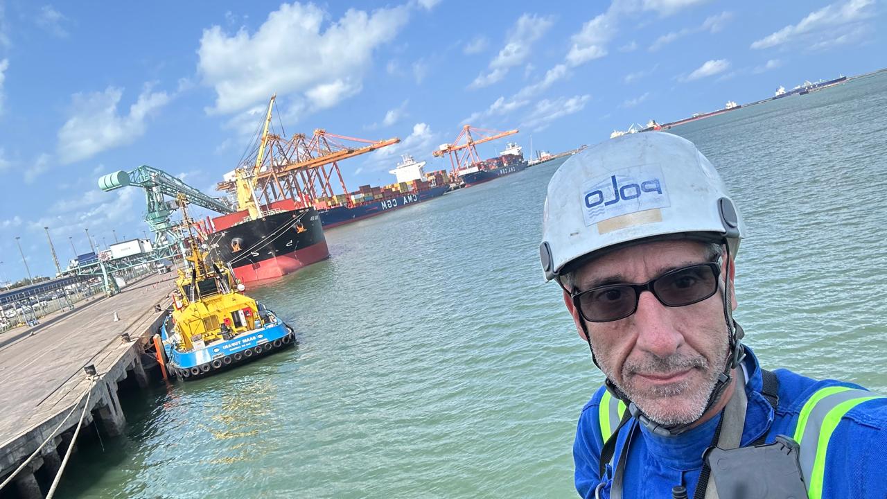 Alexandre Falcão posa para uma foto no Porto de Suape, em Pernambuco. Ele usa capacete branco, óculo