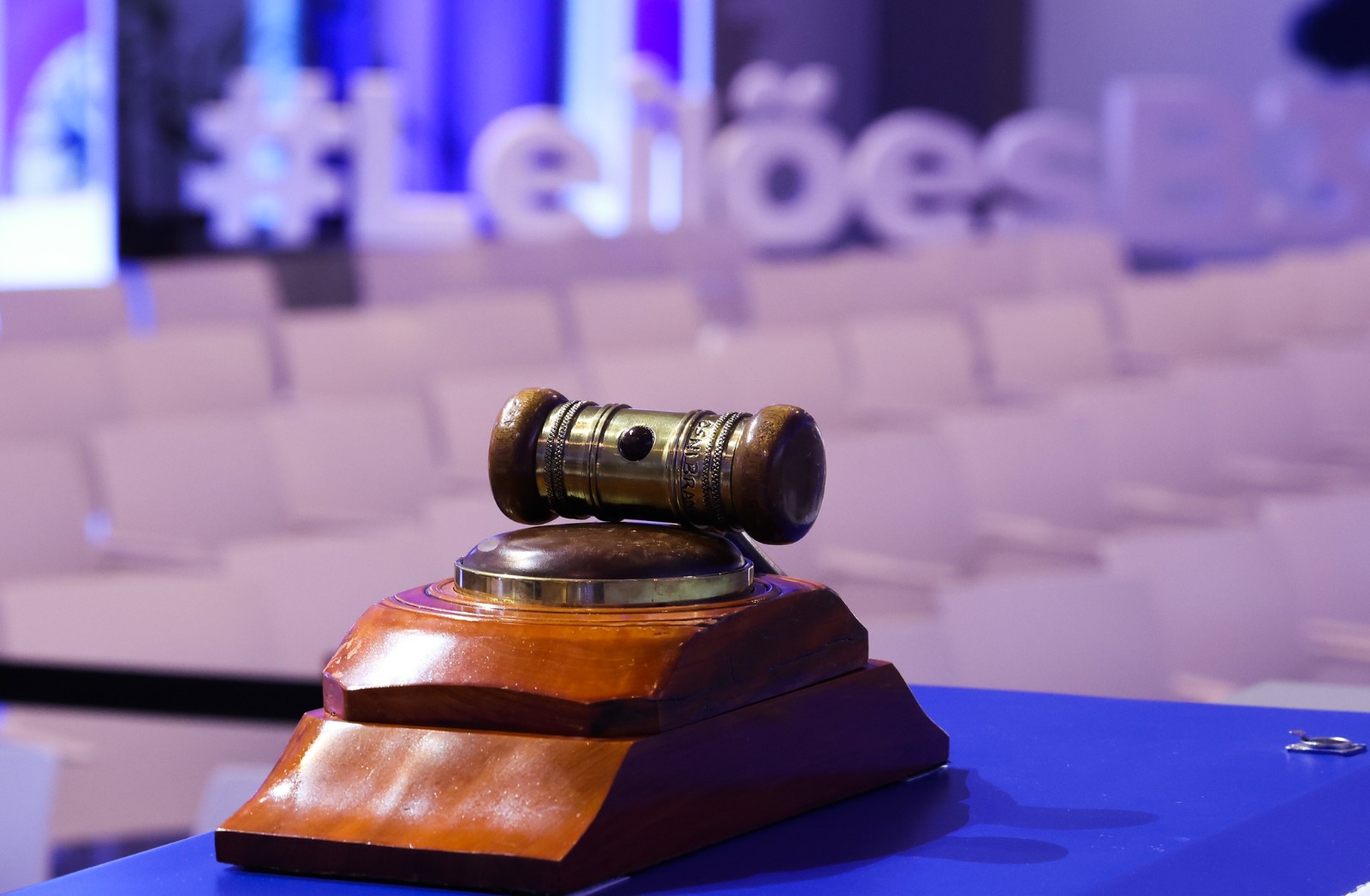Grupo de cerca de 15 pessoas, majoritariamente homens em trajes formais, reunidas no palco da bolsa de valores durante evento oficial. No centro, duas pessoas seguram juntas um martelo de madeira posicionado sobre uma bancada azul, simulando a batida de encerramento de um leilão.  Ao fundo, há um grande telão azul com o título em letras brancas: "1º Bloco de LEILÕES PORTUÁRIOS de 2026". Abaixo do título, três pequenas caixas verdes destacam as siglas das áreas leiloadas: "MCP01 | AP", "POA26 | RS" e "NAT01 | RN". Na faixa branca inferior do telão, estão estampadas as marcas da B3, ANTAQ, Ministério de Portos e Aeroportos e o logotipo do Governo do Brasil com o slogan "Do lado do povo brasileiro". As pessoas no palco sorriem e olham em direção à câmera, celebrando o momento.