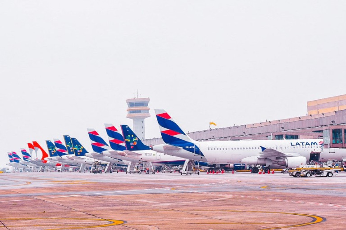 A foto mostra uma fileira organizada de aviões comerciais estacionados no pátio de um aeroporto em u