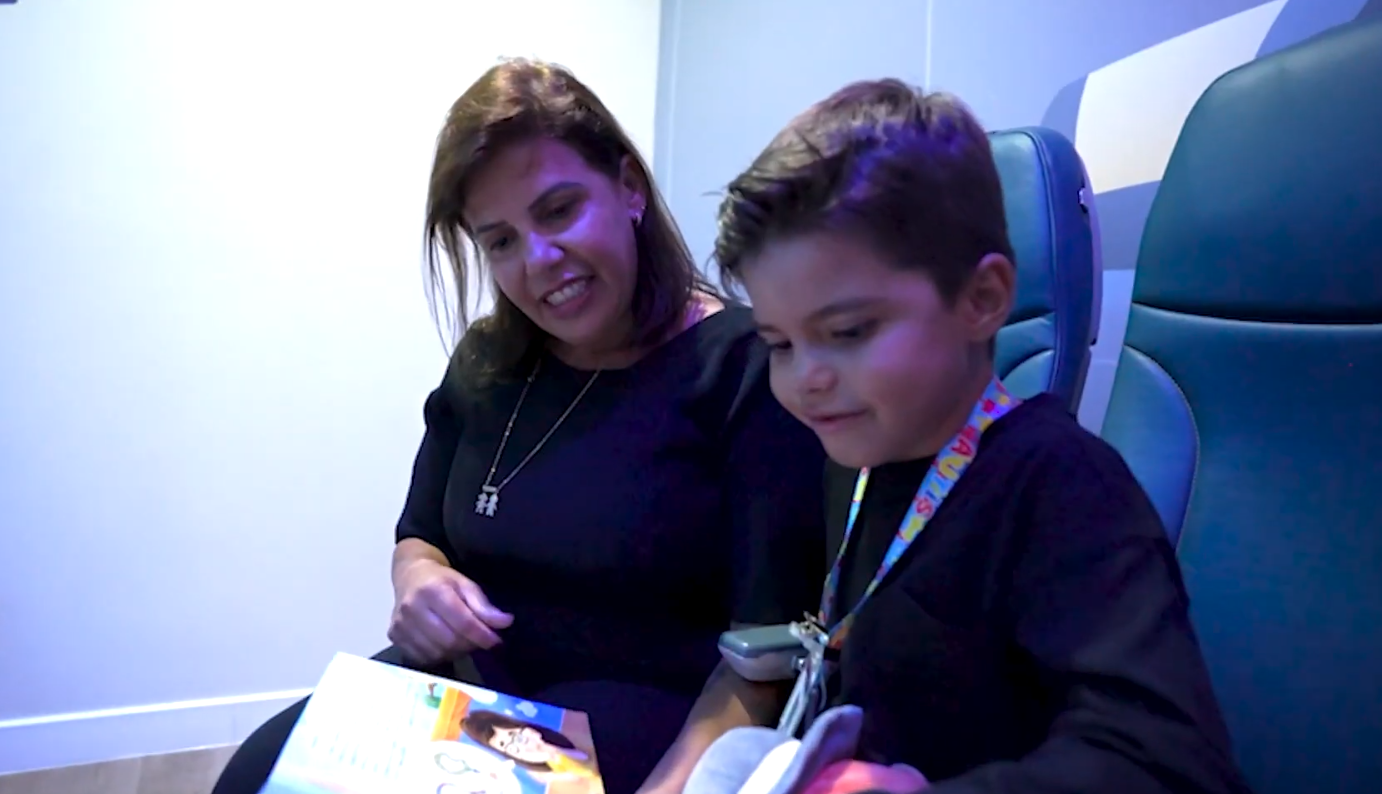 Mãe e filho sentados em poltronas de avião folheiam um livro