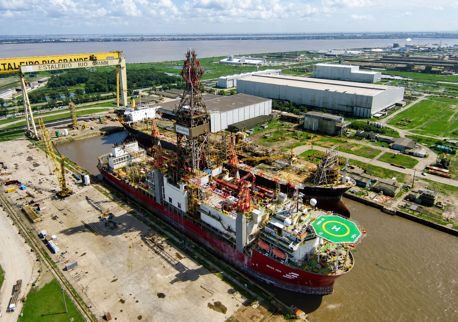 Vista aérea de estaleiro naval com navio em construção às margens de um rio.