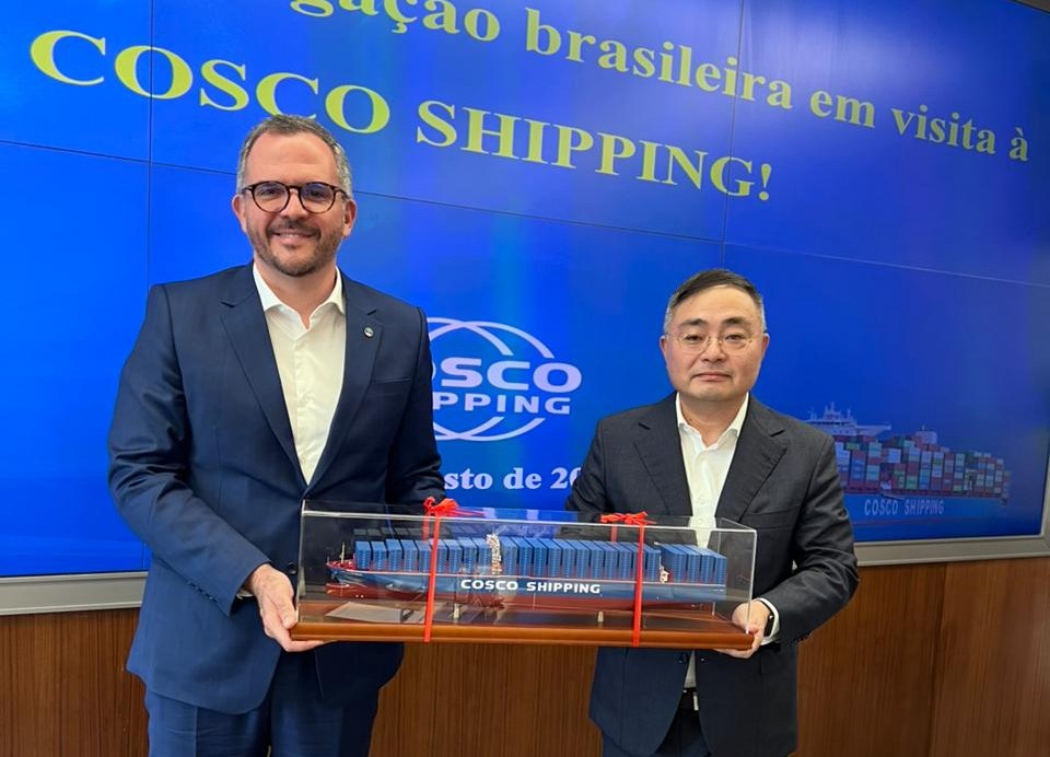 Dois homens, usando terno azul marinho, assinam documentos,