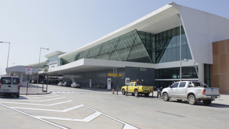 Vista externa do terminal de passageiros do Aeroporto Internacional de Manaus, com veículos na área de embarque e desembarque.