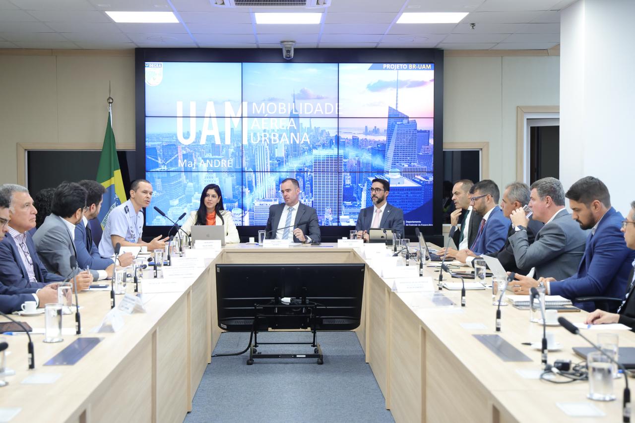 Foto mostra sala de reuniões, com representantes e autoridades sentadas à mesa que possui formato de "U".
