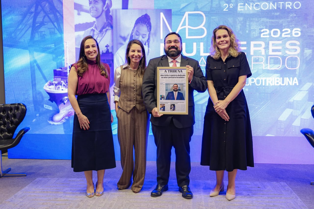 Secretário Alex segurando uma moldura com a homenagem na capa exclusiva do jornal A Tribuna, durante o evento Mulheres a Bordo.