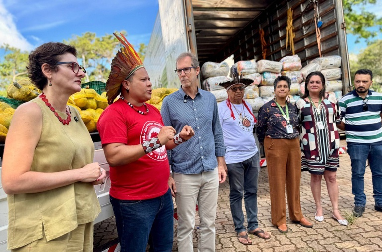 Kleber Karipuna, coordenador executivo da APIB, dialoga com representantes da CONAB em frente a um caminhão com o baú repleto de cestas básicas.