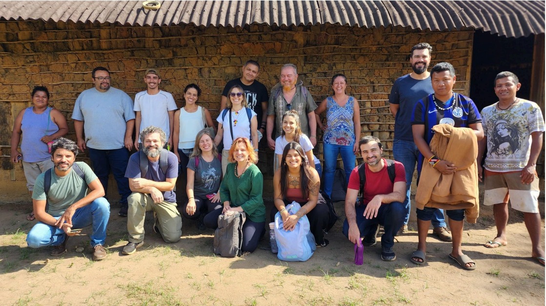 Grupo de representantes do  governo e da UFSCAR posam para foto com casa de  sapê ao fundo
