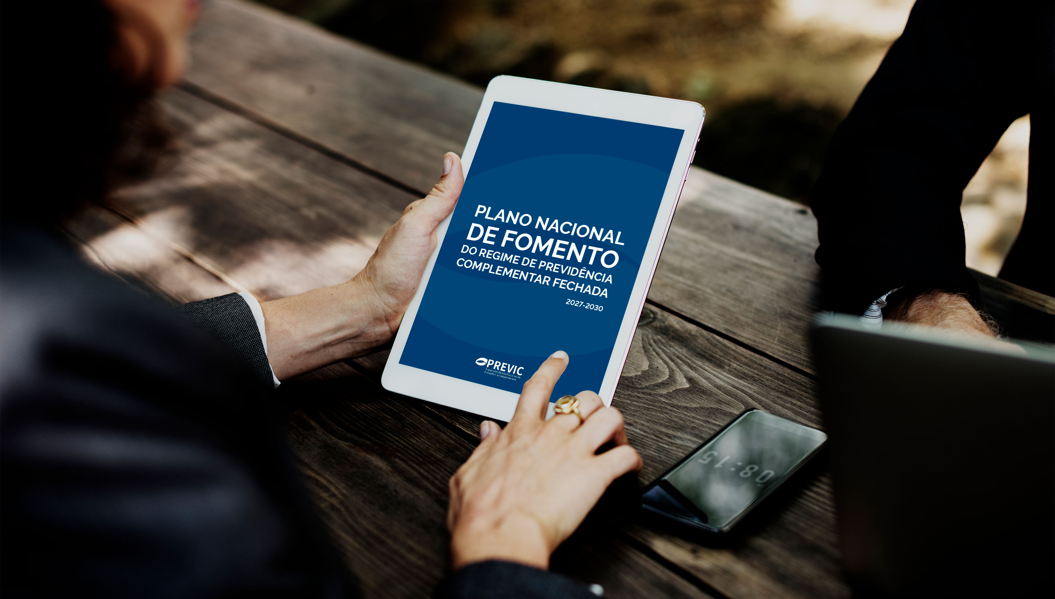 Pessoa segura um tablet exibindo a capa do Plano Nacional de Fomento da PREVIC