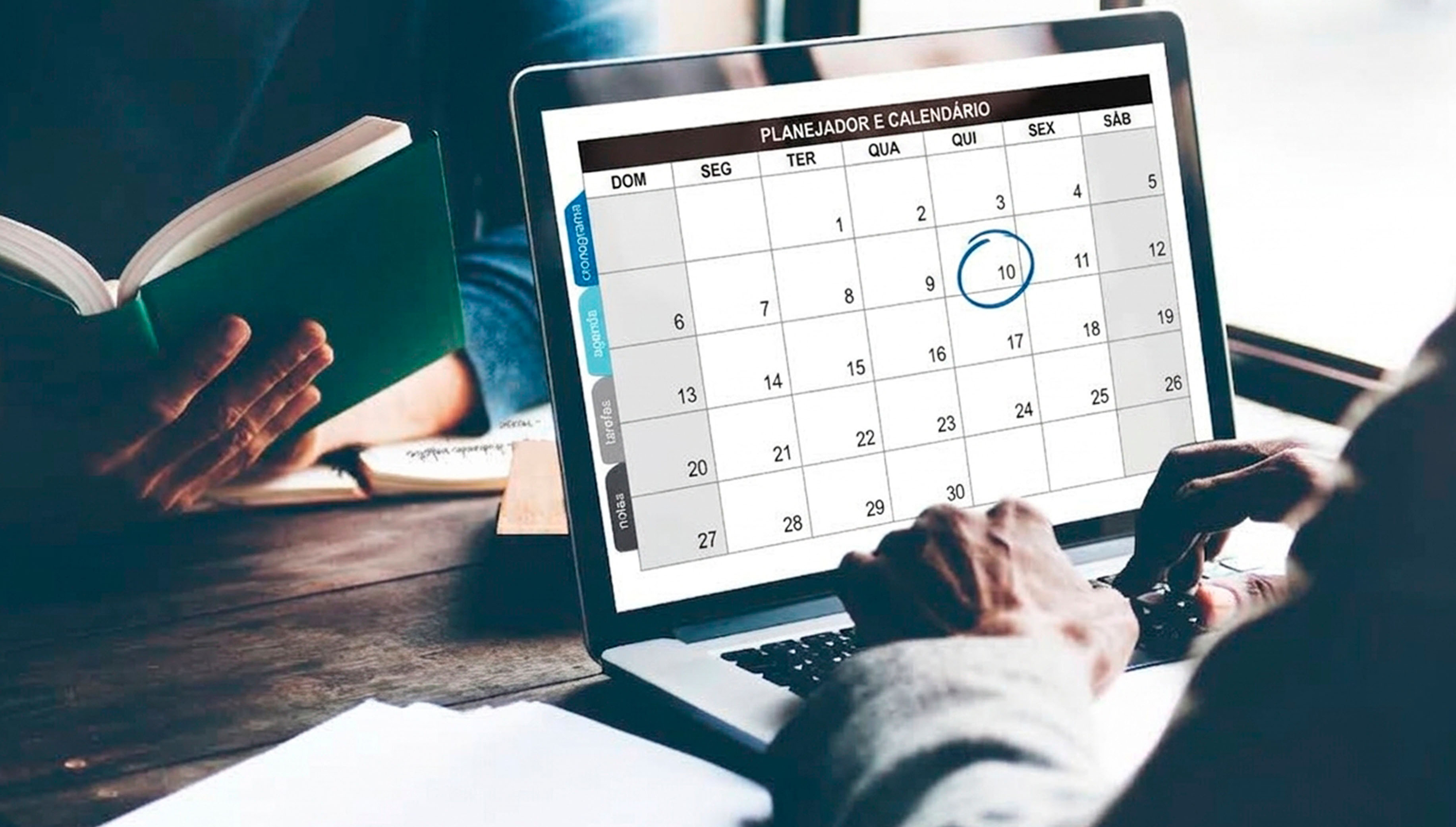 Pessoa digita em computador com calendário na tela, enquanto outra segura livro aberto