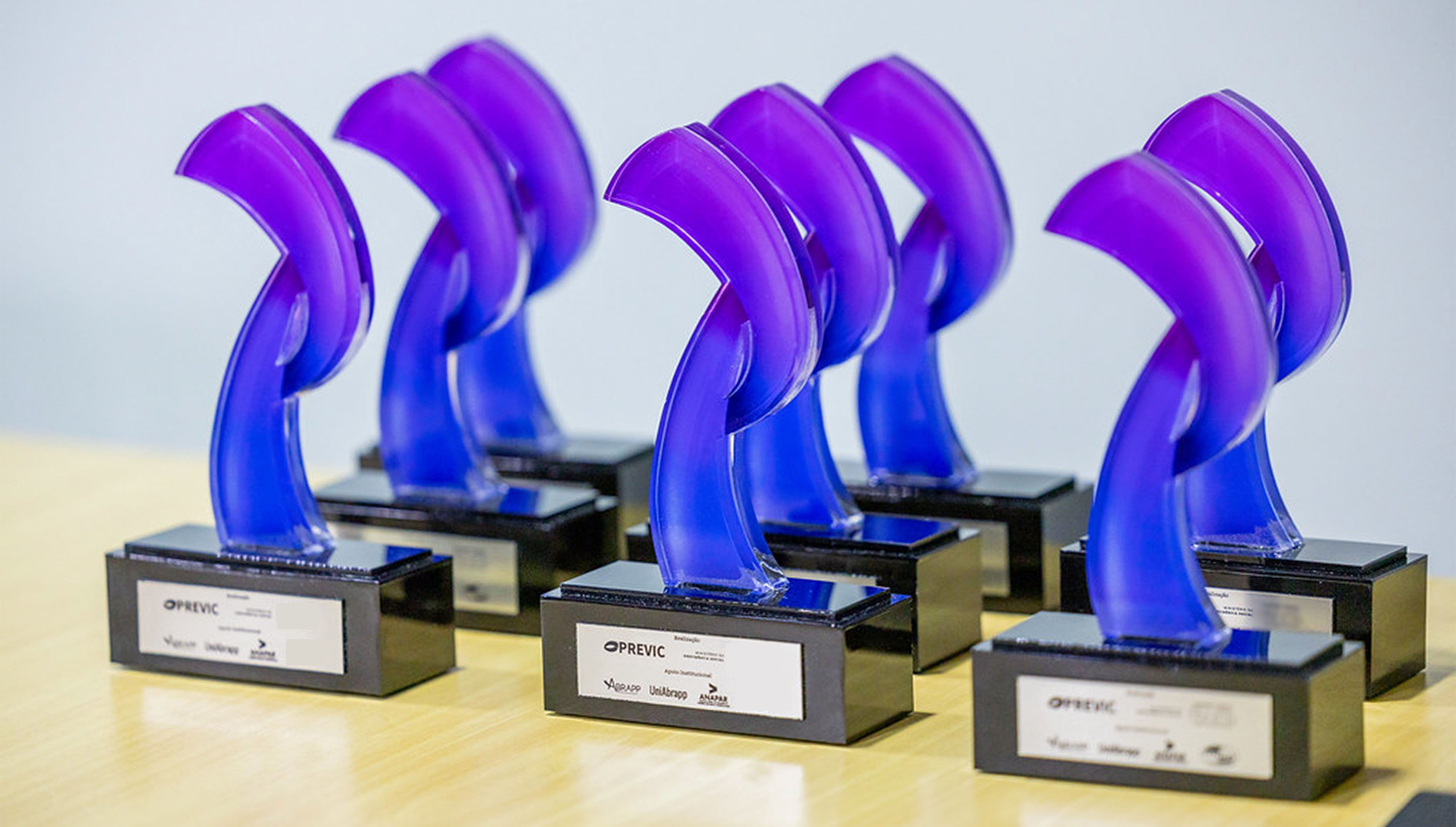 Troféu do 10º Prêmio PREVIC...: Troféus de acrílico roxo e azul dispostos em uma mesa.