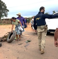 A imagem mostra um policial rodoviário federal garantindo a segurança da situação enquanto os manifestantes retiram objetos da via