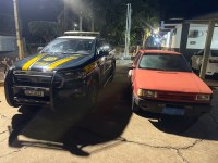 A imagem mostra dois carros, uma viatura da PRF e um Fiat/Elba vermelho, estacionados lado a lado à noite