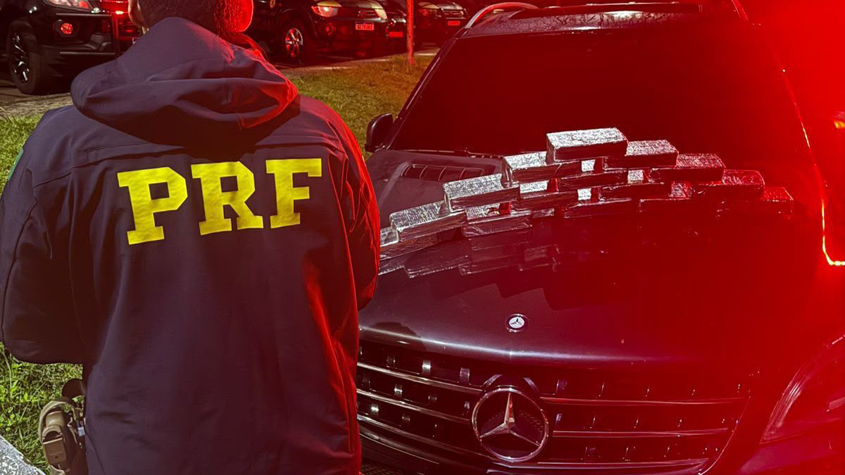 Policial em frente a veículo com drogas empilhadas sobre o capô