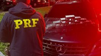 Policial em frente a veículo com drogas empilhadas sobre o capô