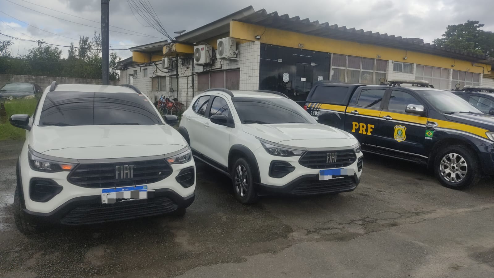 A imagem apresenta dois carros idêncitoc s ao lado de uma viatura da PRF