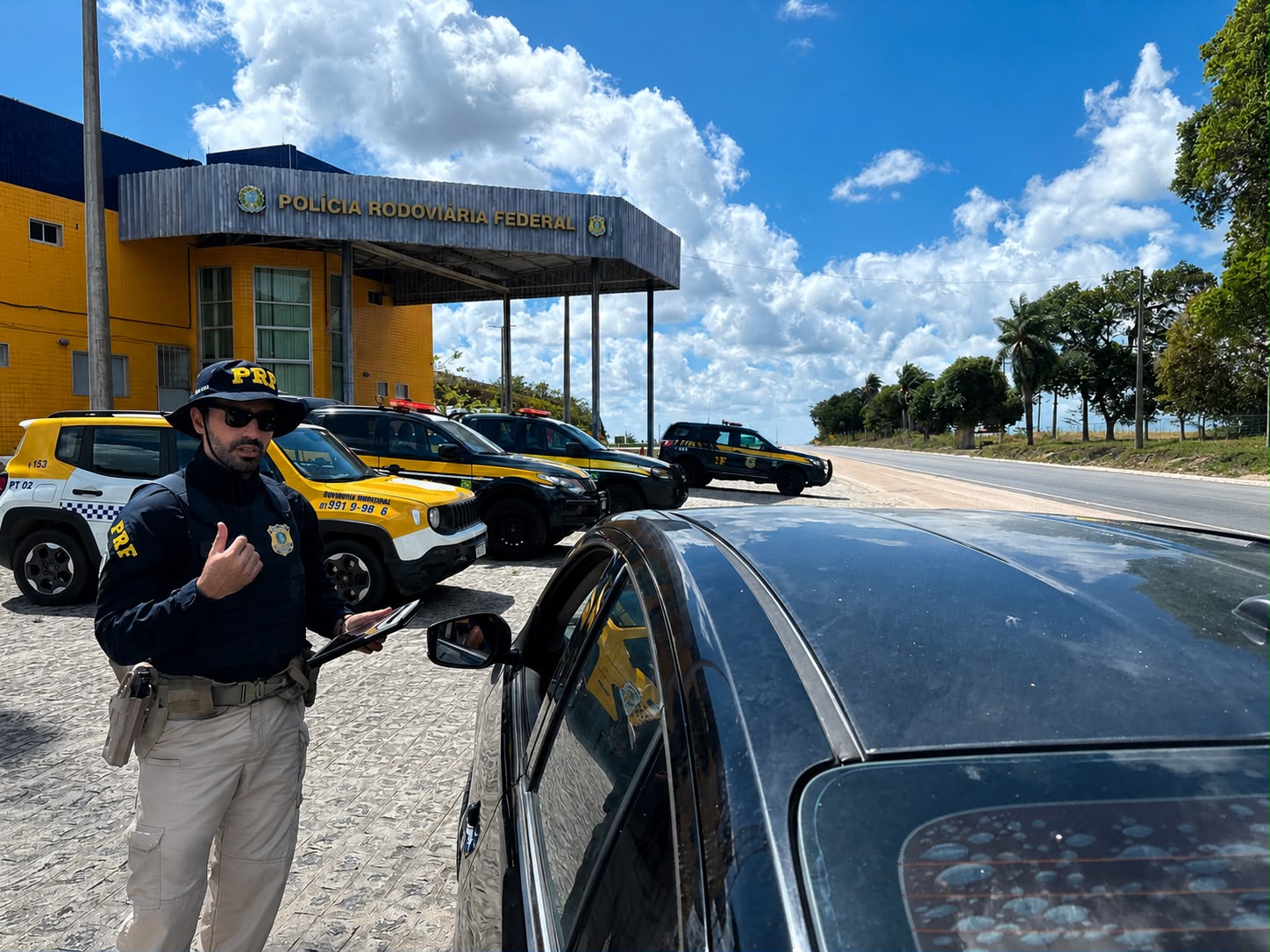 Agente da PRF realiza atendimento a motorista em frente a uma unidade da Polícia Rodoviária Federal.