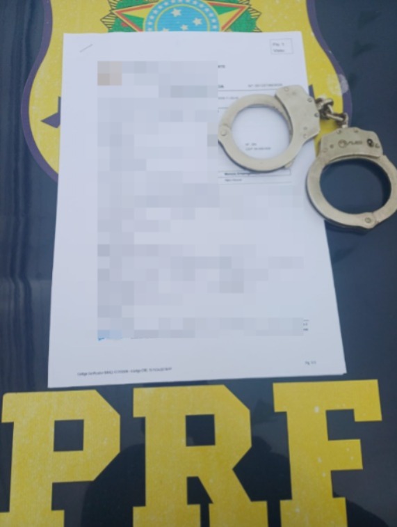 Mandado de prisão impresso com uma algema ao lado em cima do capô da viatura da PRF