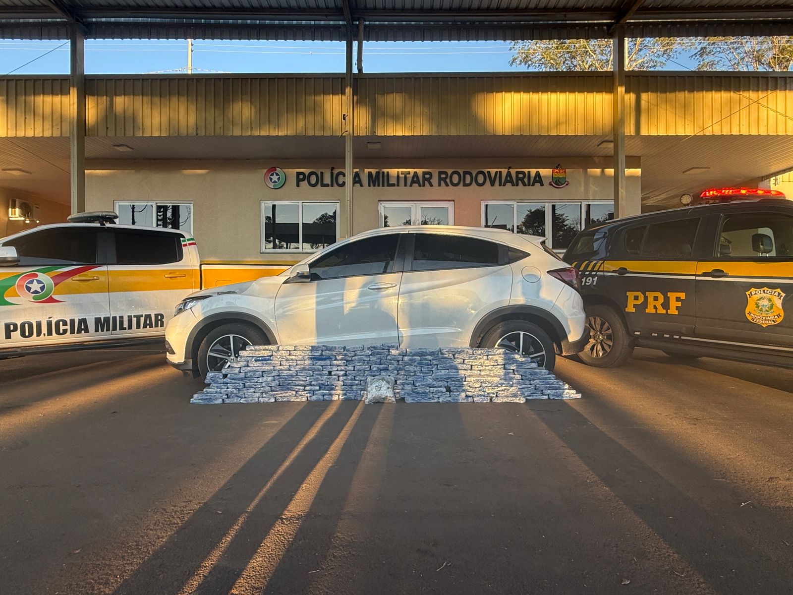 Carro apreendidos com as drogas ao lado das viaturas da PRF e da PMRv