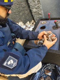 Policial rodoviário federal remove volumes de haxixe encontrados em compartimentos ocultos durante inspeção veicular.
